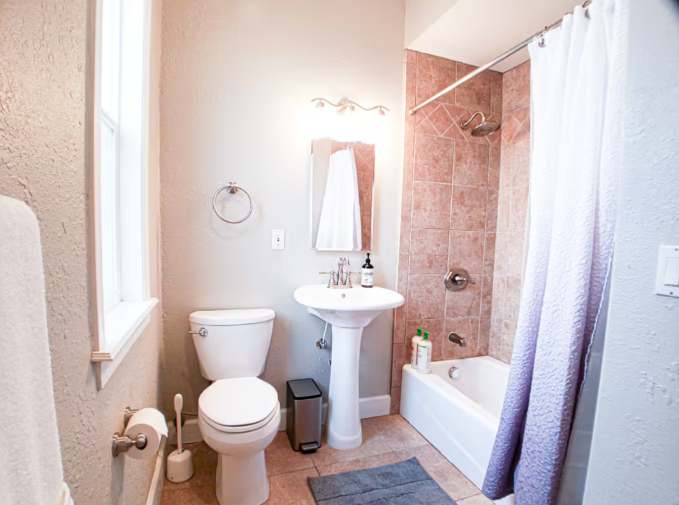 Bright bathroom with pedestal sink, tub-shower combo, and pink tile