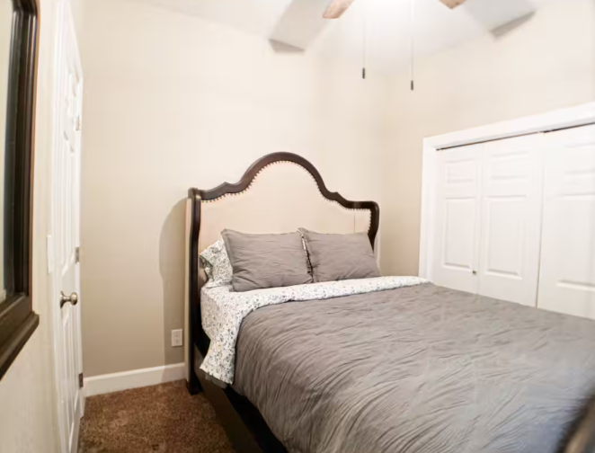 Bedroom with ornate arched headboard, gray bedding, and ceiling fan