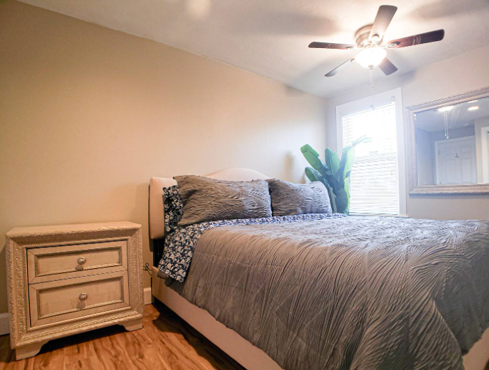Spacious master bedroom with upholstered headboard, wall-mounted TV, and sitting chairs
