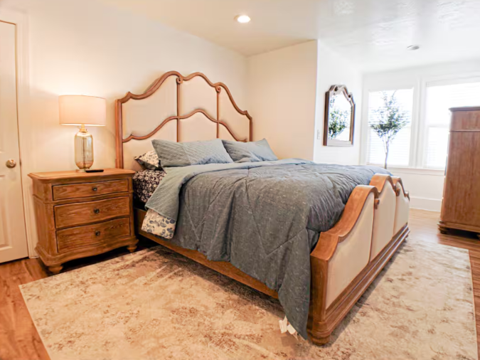 Elegant bedroom with carved wood headboard, blue bedding, nightstand, and arched mirror