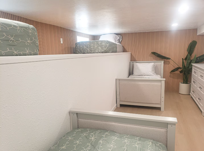 Bunk room with upper loft beds, wood slat accent wall, and plant decor