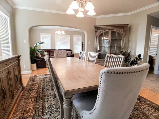 Formal dining room with large farmhouse table, upholstered chairs, and arched doorway to living room