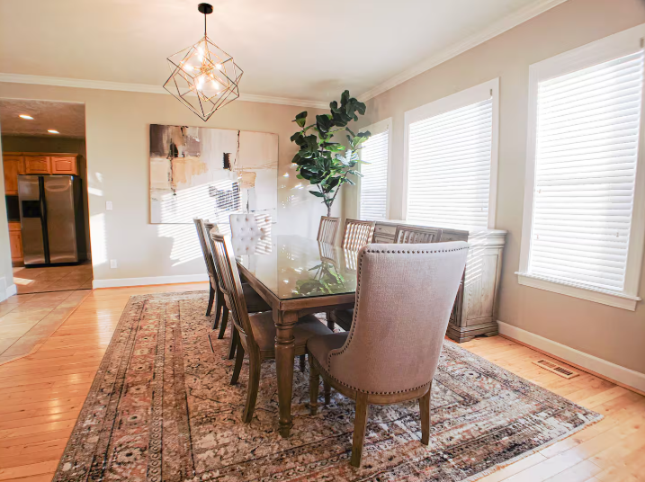 Bright dining room with glass-top table, upholstered chairs, geometric chandelier, and fiddle leaf fig