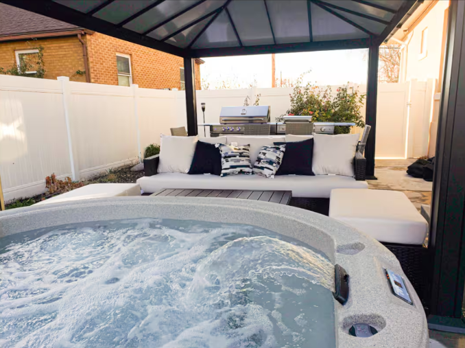 Bubbling hot tub under pergola with outdoor lounge seating and grill