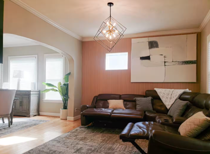 Living room with dark leather reclining sofas, geometric chandelier, and striped accent wall