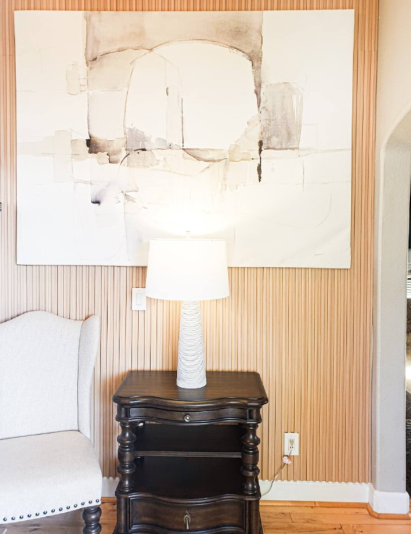 Lounge nook with vertical wood slat accent wall, abstract art, and dark wood side table