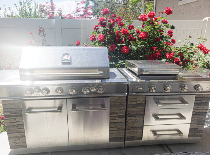 Stainless steel outdoor kitchen with dual grills and red rose garden backdrop