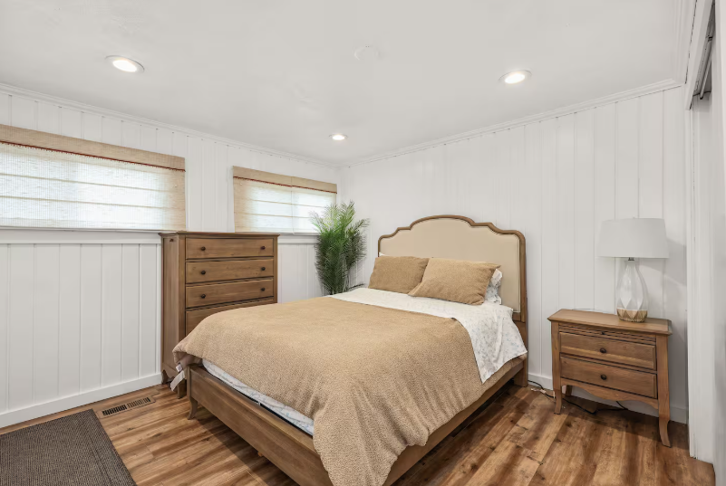 Queen bedroom with upholstered headboard, dresser and palm plant