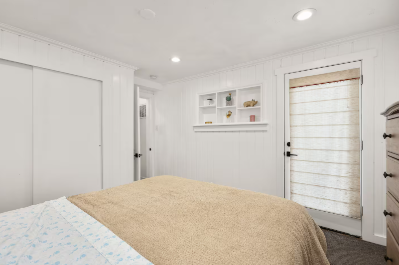 Bright queen bedroom with built-in shelving and roman shades
